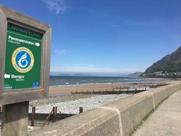 Llanfairfechan's promenade and sandy beach pictured with a sign in the foreground
