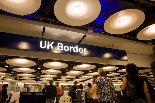 Image of travellers passing through sign that says UK Border at Heathrow Airport