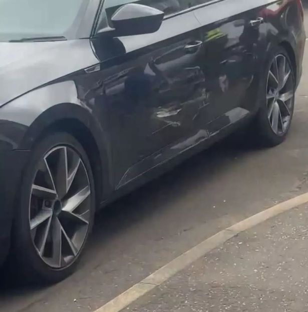 An image of the side of a black car, which is dented and scratched.