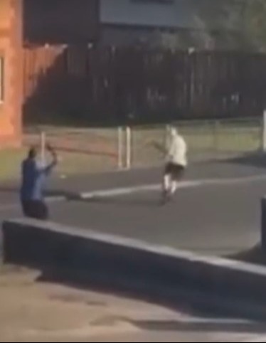Two people fighting with large knives in a street.
