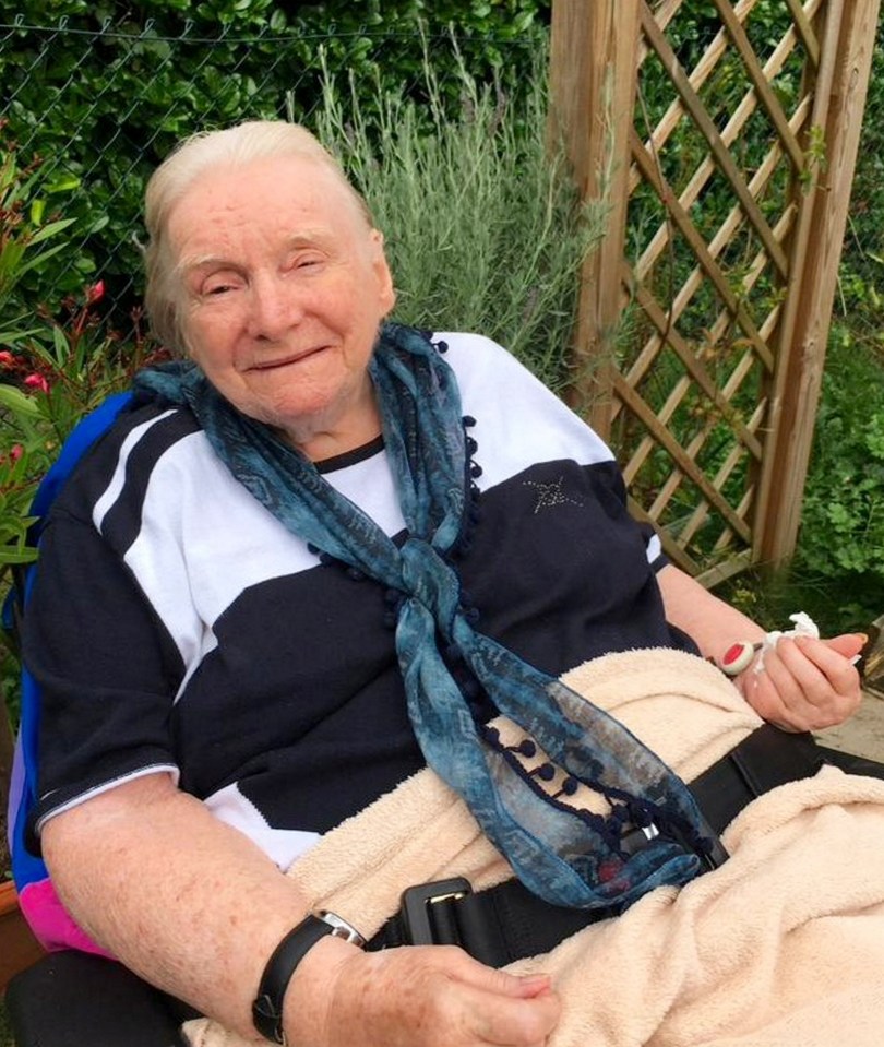 Elderly woman sitting outdoors smiling.