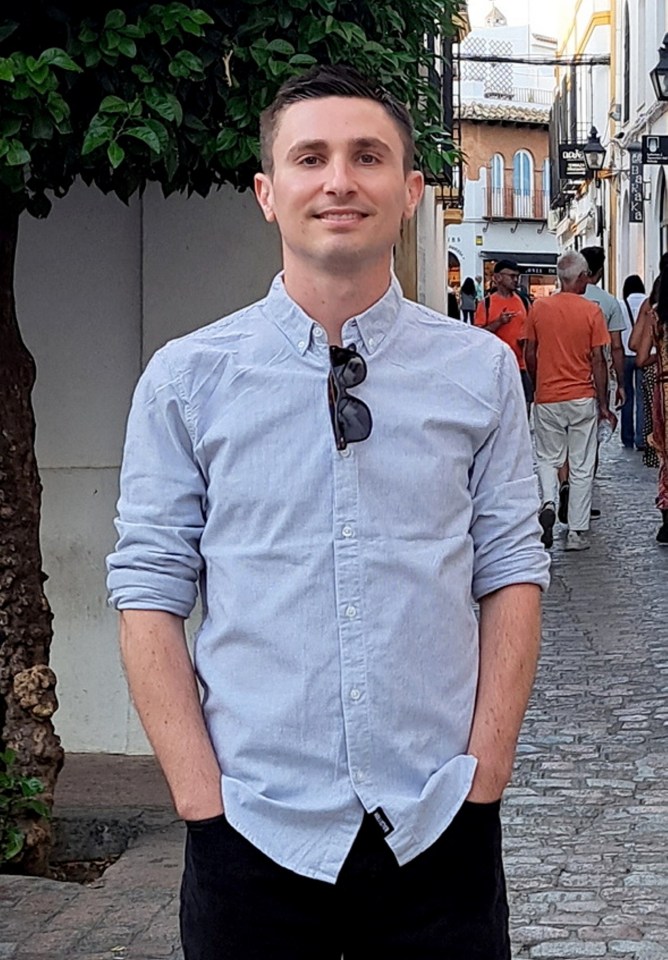 Man in light blue shirt standing on cobblestone street.