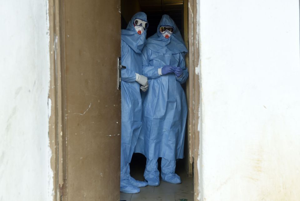 Two healthcare workers in protective gear stand in a doorway.
