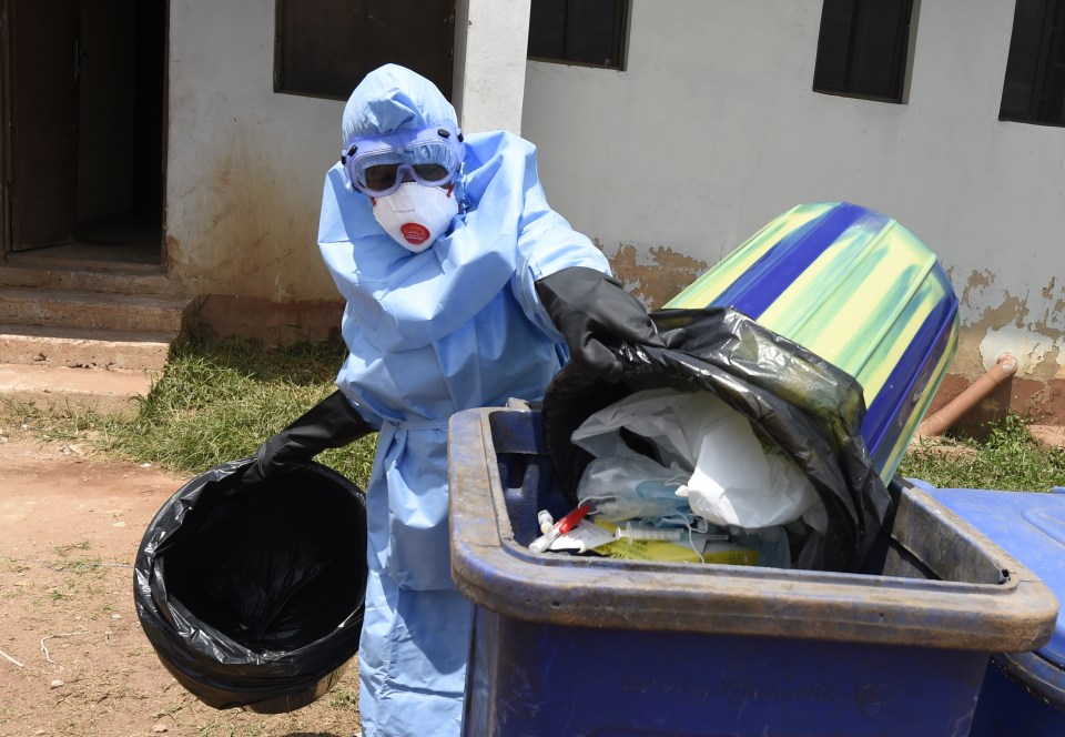 A health official in protective gear disposes of medical waste.