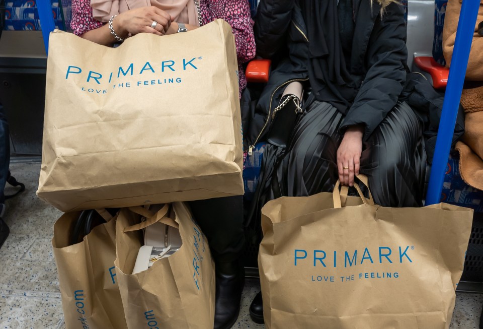 Two people on a train carrying multiple Primark shopping bags.