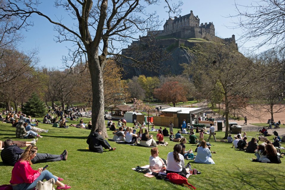 People enjoying a sunny day in a park with Edinburgh Castle in the background.