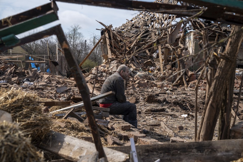 Man sits amidst the rubble of a bomb-damaged building.