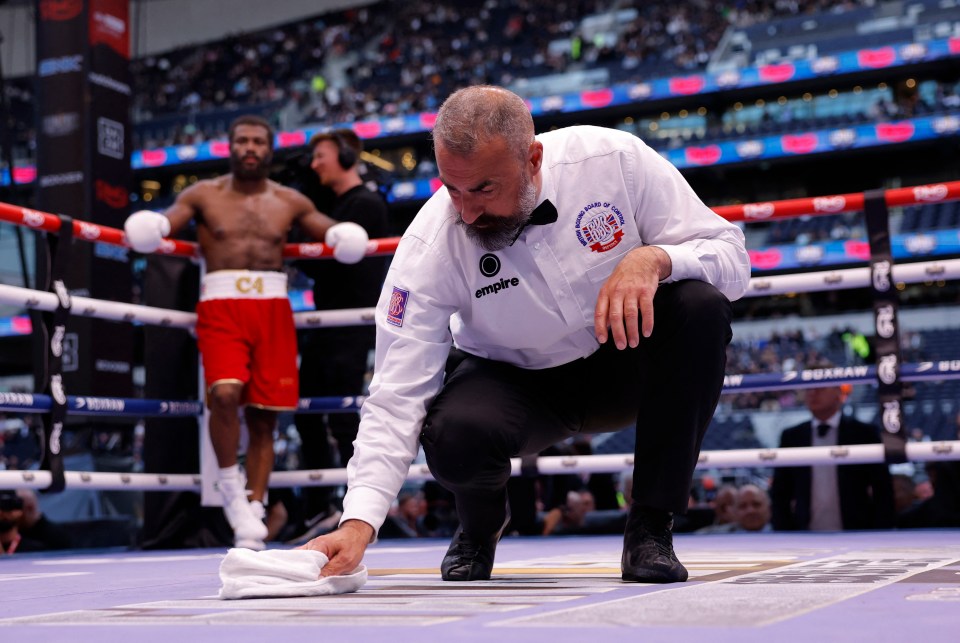 A boxing referee wipes the canvas of the ring.