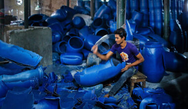 A man employed in a plastic recycling plant breaks down plastic barrels