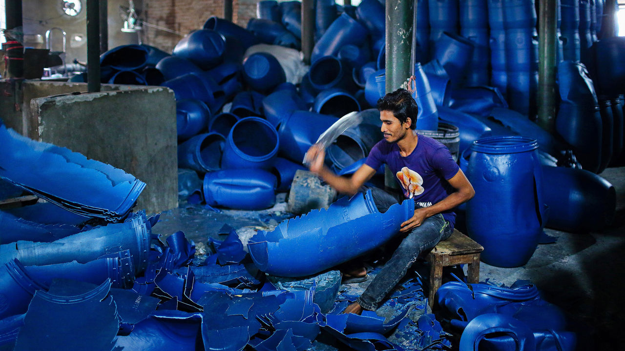 A man employed in a plastic recycling plant breaks down plastic barrels