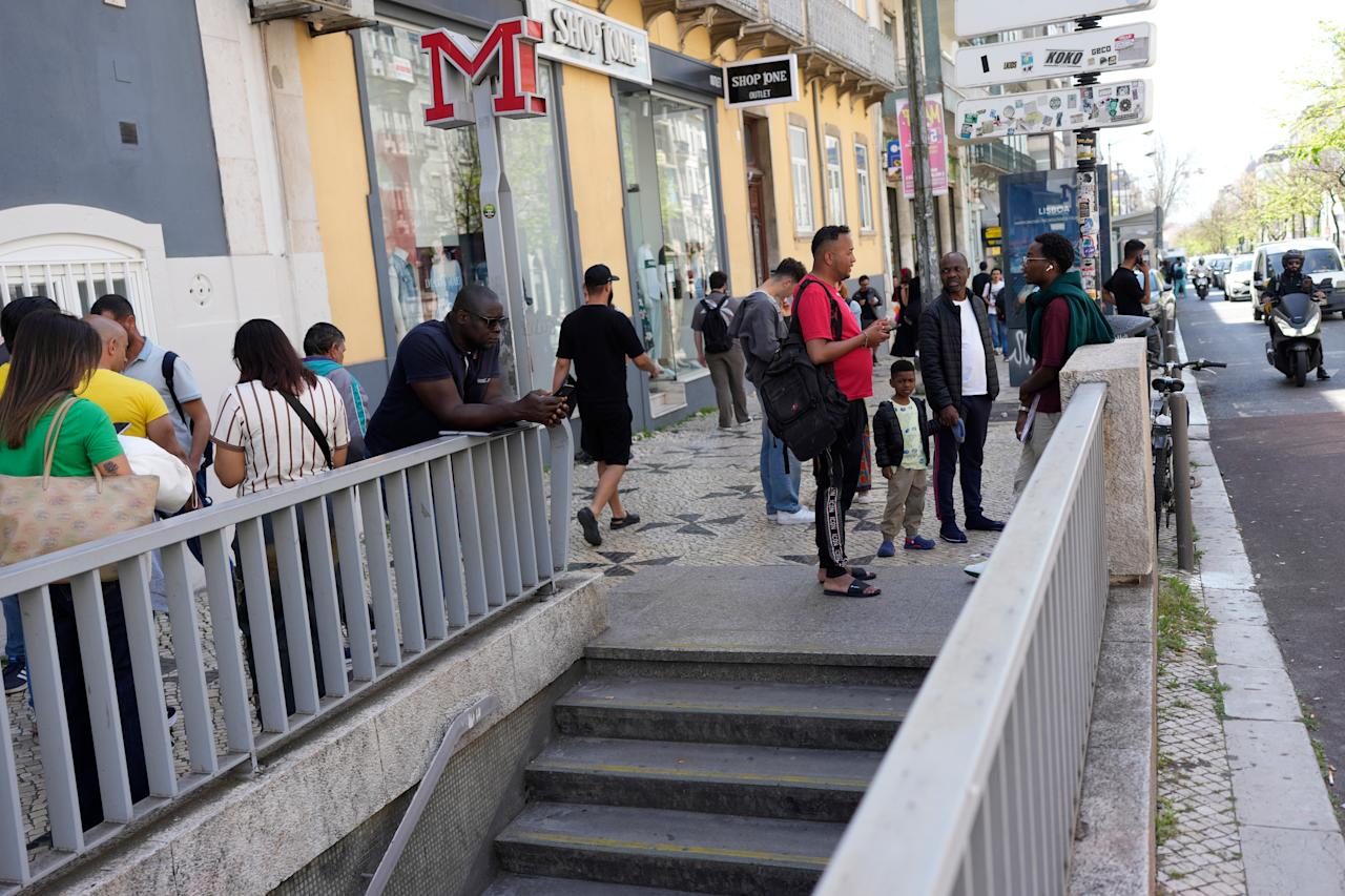 People check their mobile phones as they stand outside a closed subway station following a power outage in Lisbon, Portugal, Monday, April 28, 2025. (AP Photo/Armando Franca)