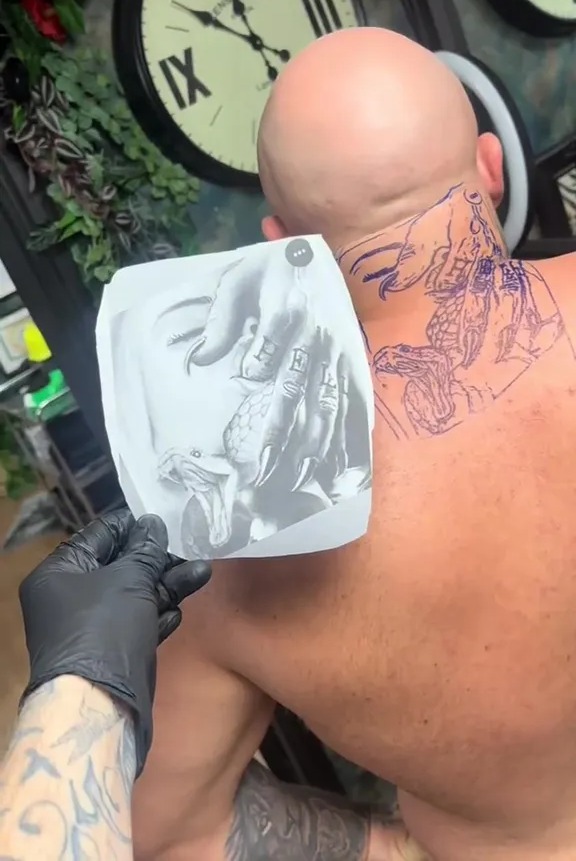 Stencil of a hand and snakes being applied to a man's neck for a tattoo.