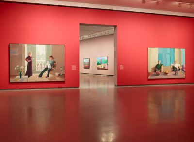 View of an art museum with vermillion-painted walls and two double portraits on the wall in front of an entry way. 