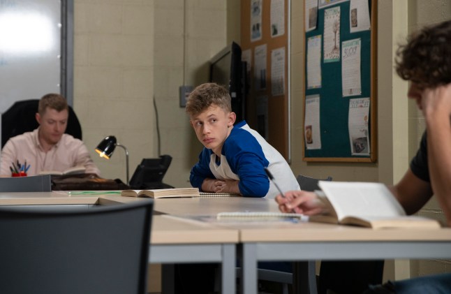 Dylan leans forward on a classroom table in Corrie