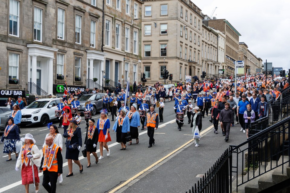 A parade of people in orange and blue uniforms marching down a city street.