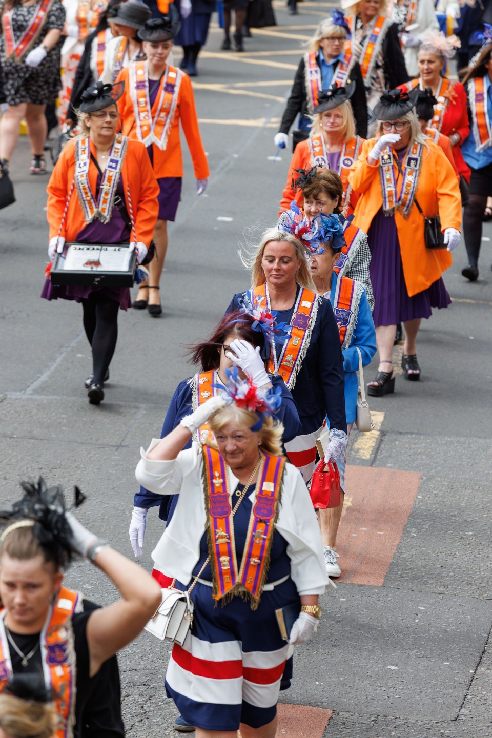 Women in orange sashes and hats walking in a parade.