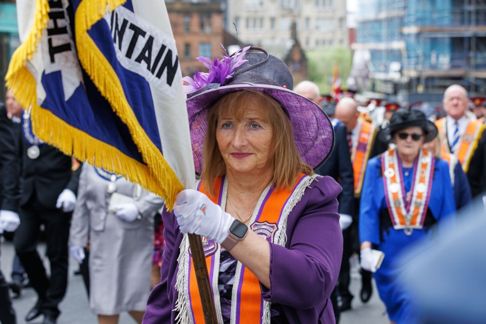 Woman in purple carrying an Orange Order banner.