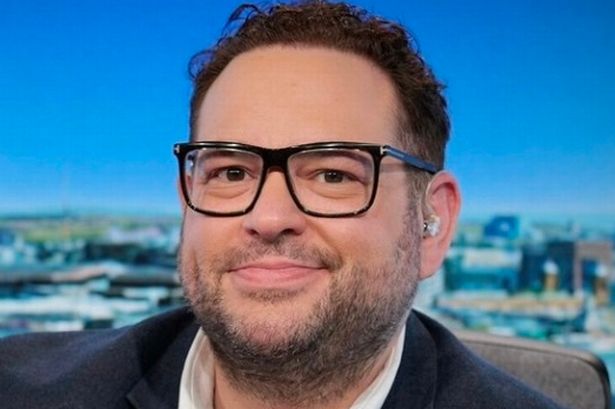 A head shot of Cristo Foufas in front of a radio microphone