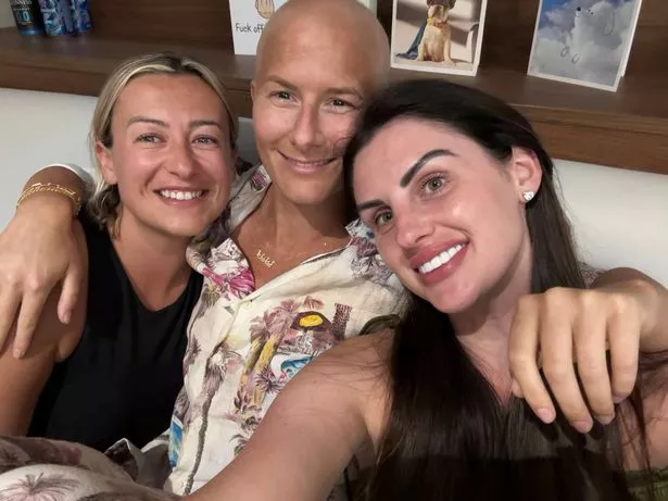 Olivia, dressed in a white shirt, hugging her two best friends