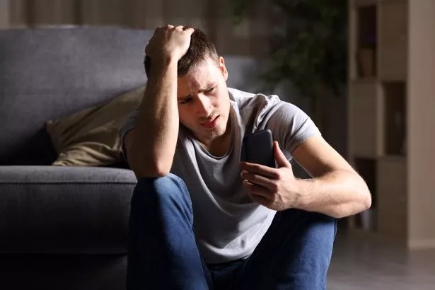 A stock shot of a man looking unhappy sitting on the floor of a darkened room