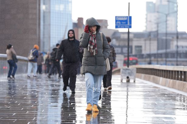 People shelter from the rain as they walk across London Bridge in central London