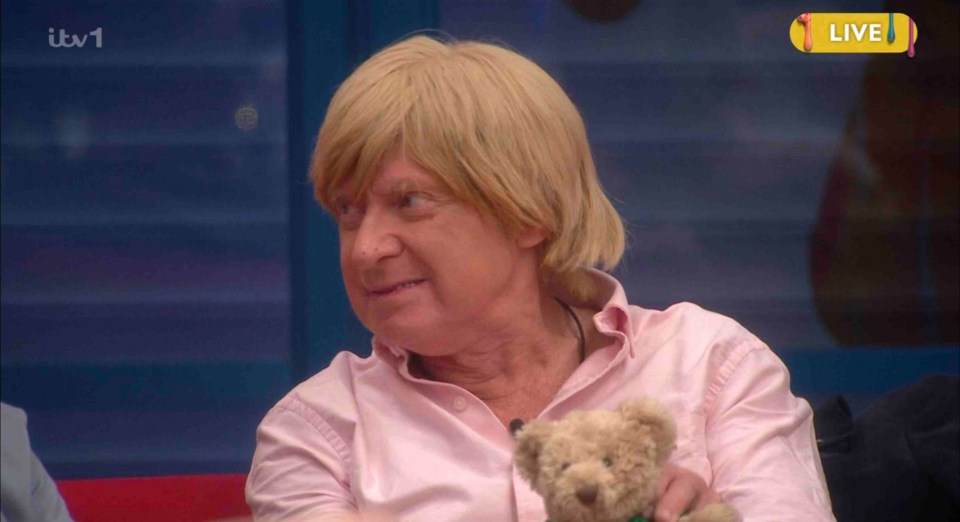 Man with blond wig holding teddy bear.