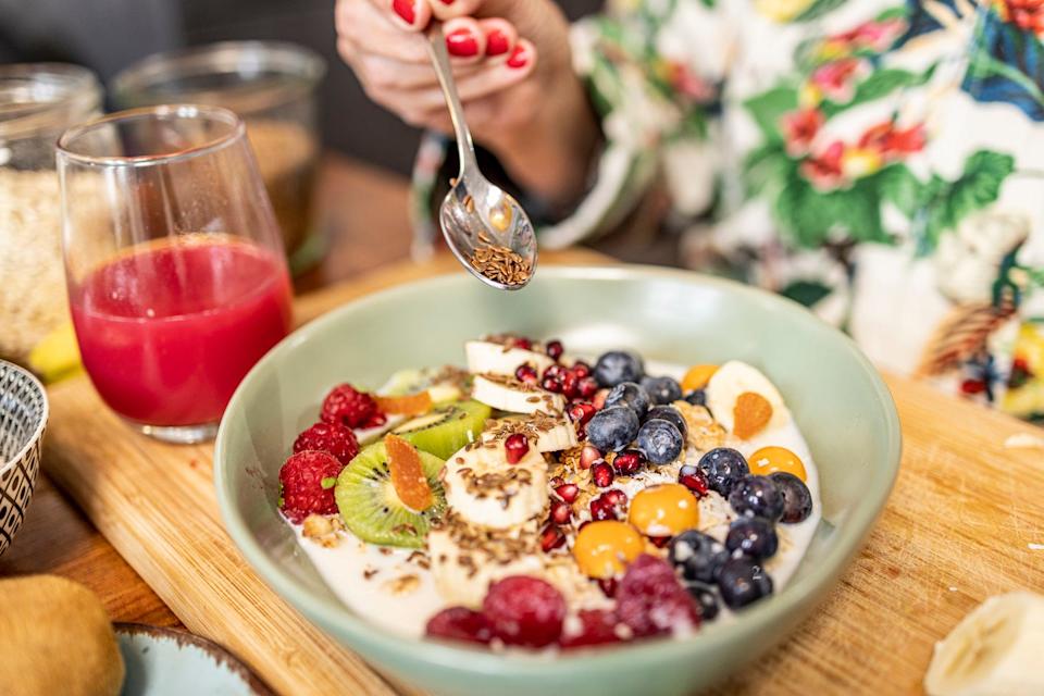spoon of flaxseeds being dumped into bowl of yogurt and fruit