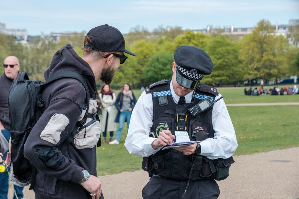 A police officer writing in a notebook while speaking to a person with a backpack at a 420 cannabis celebration.