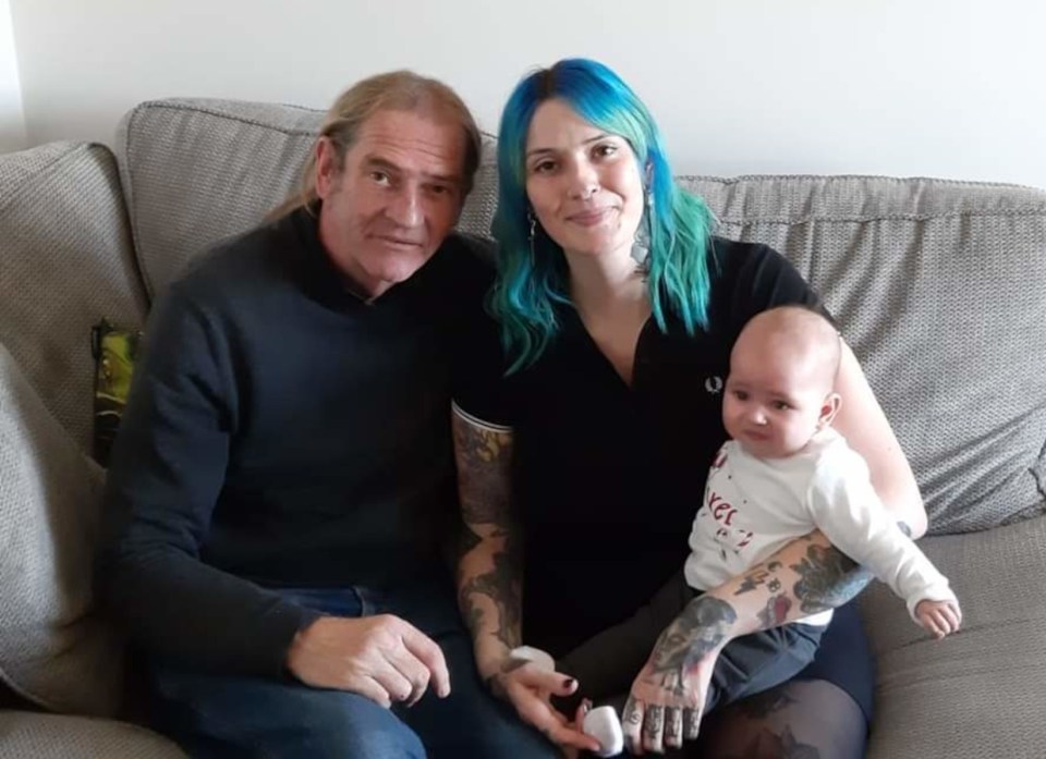 A man and woman sit on a couch with their baby.