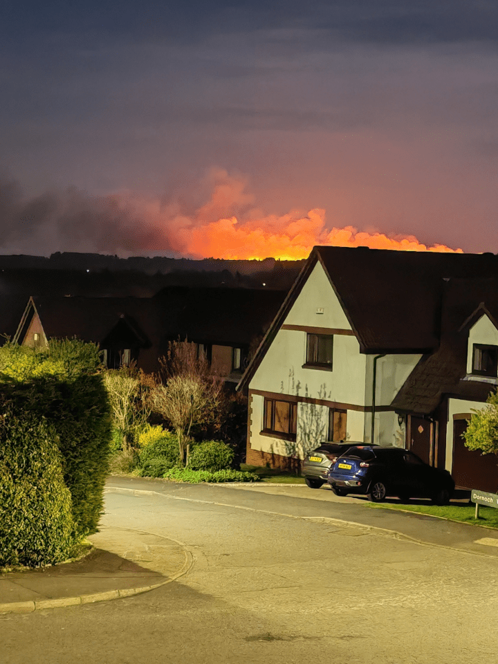 Houses at night with a large fire in the distance.