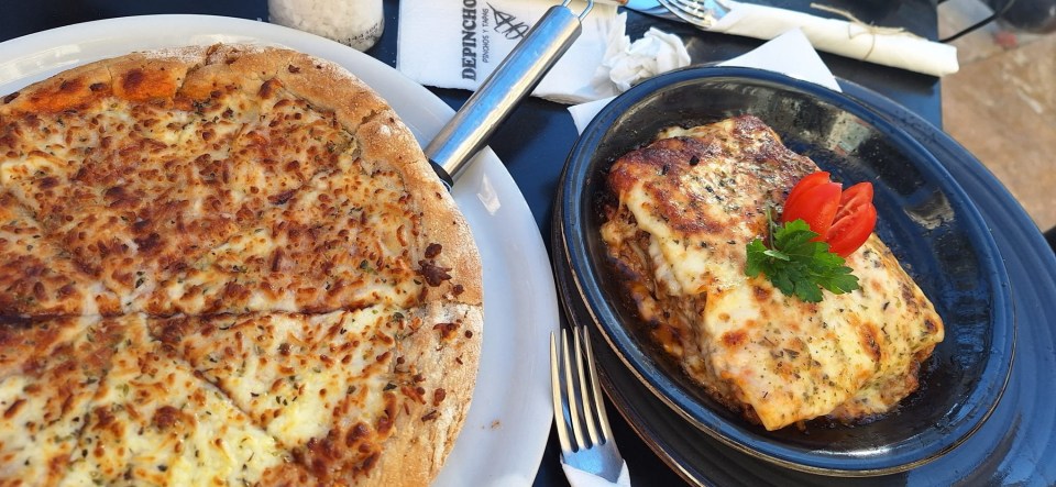 Pizza and lasagna on plates at a restaurant table.
