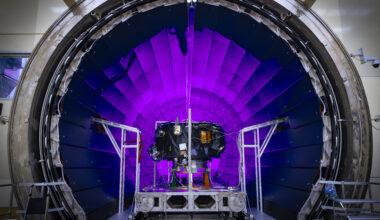 A tunnel dramatically lit in violet light dominates the photo. In front of it, a small spacecraft is on a track.