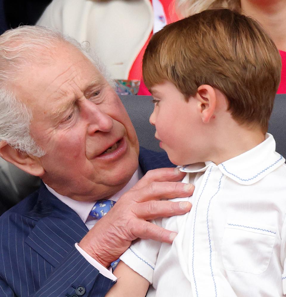  King Charles sitting in a chair wearing a blue suit and a blue tie with Prince Louis, dressed in a white shirt, on his lap . 