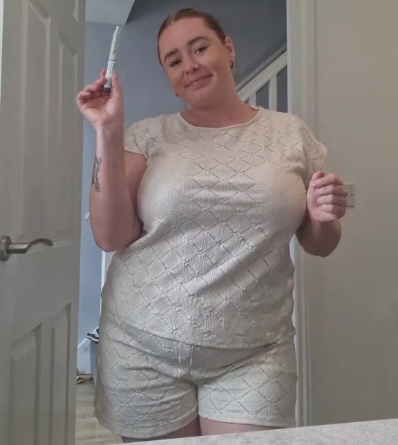 Woman in a white outfit holding a pregnancy test.