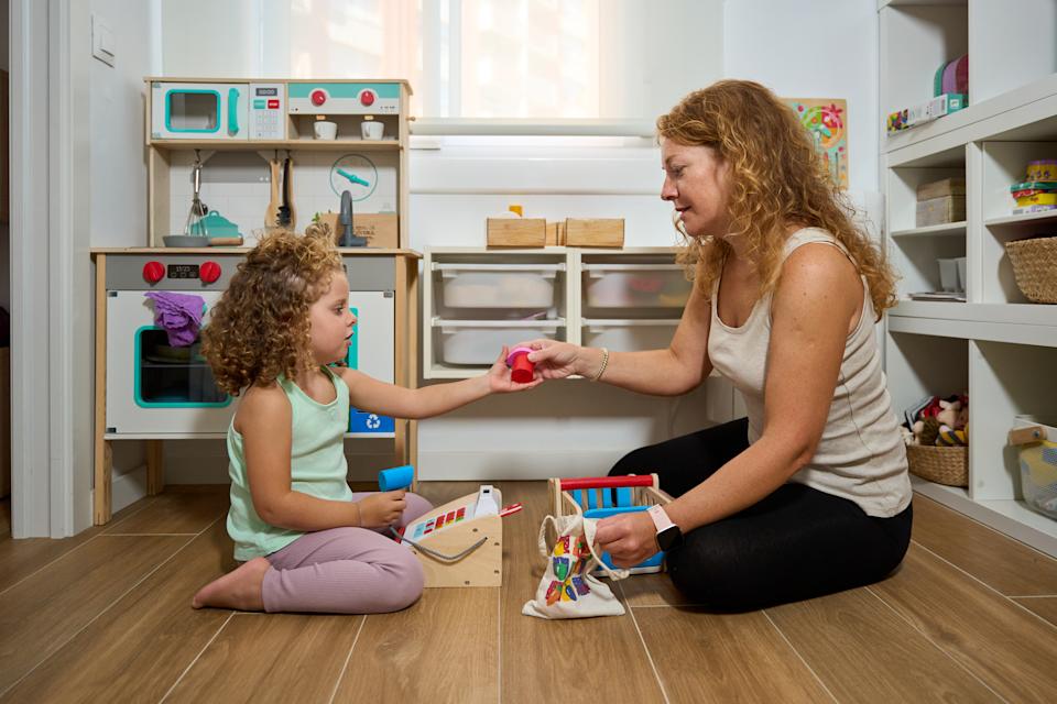 Little girl playing store with her educator, using wooden toys in a kindergarten room, promoting early learning and development