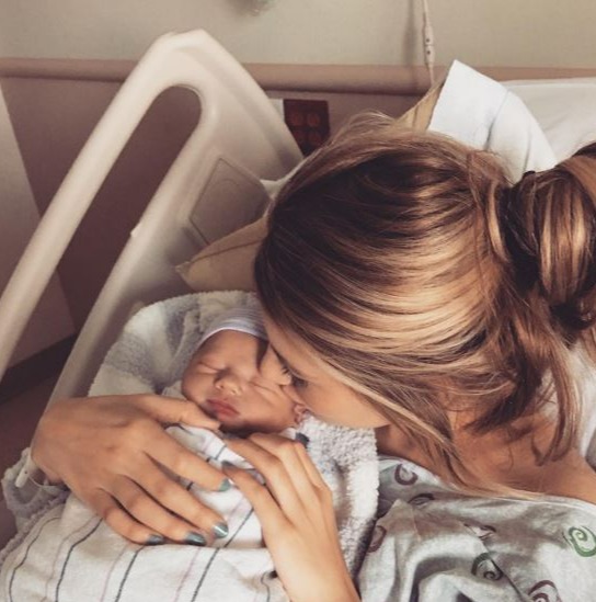 Mother kissing newborn baby in hospital.