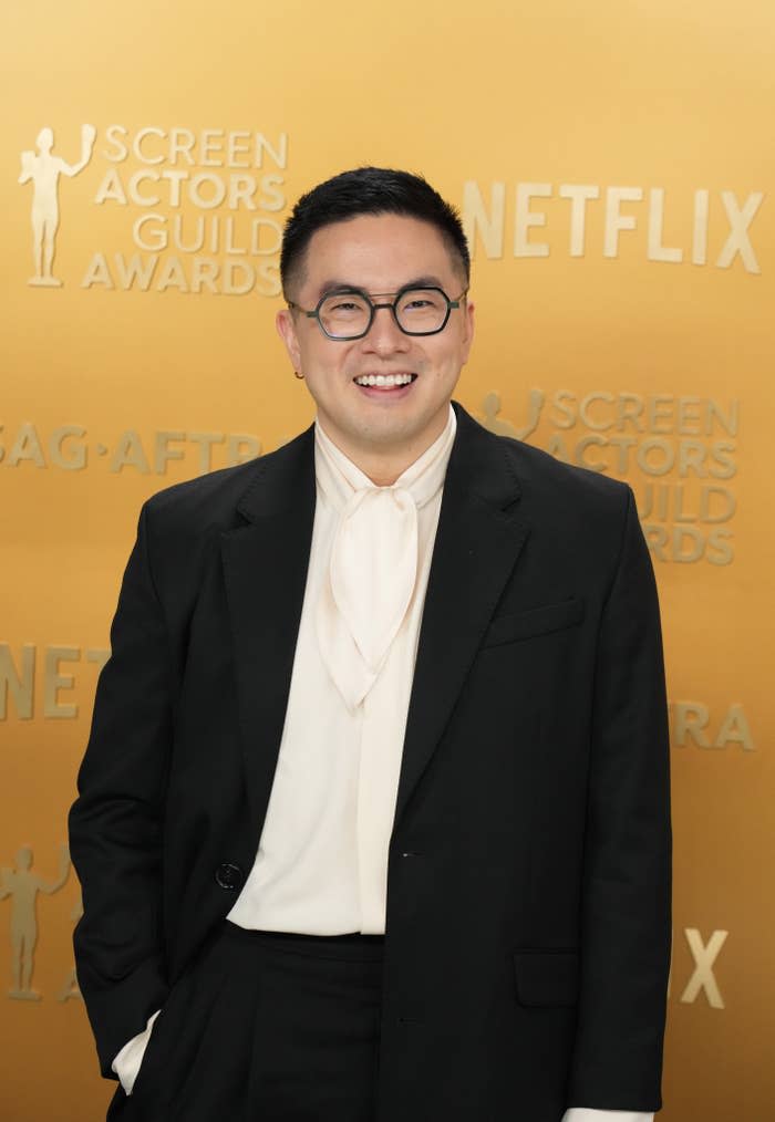 Bowen Yang smiles on the SAG Awards red carpet, wearing a classic black suit with a white shirt