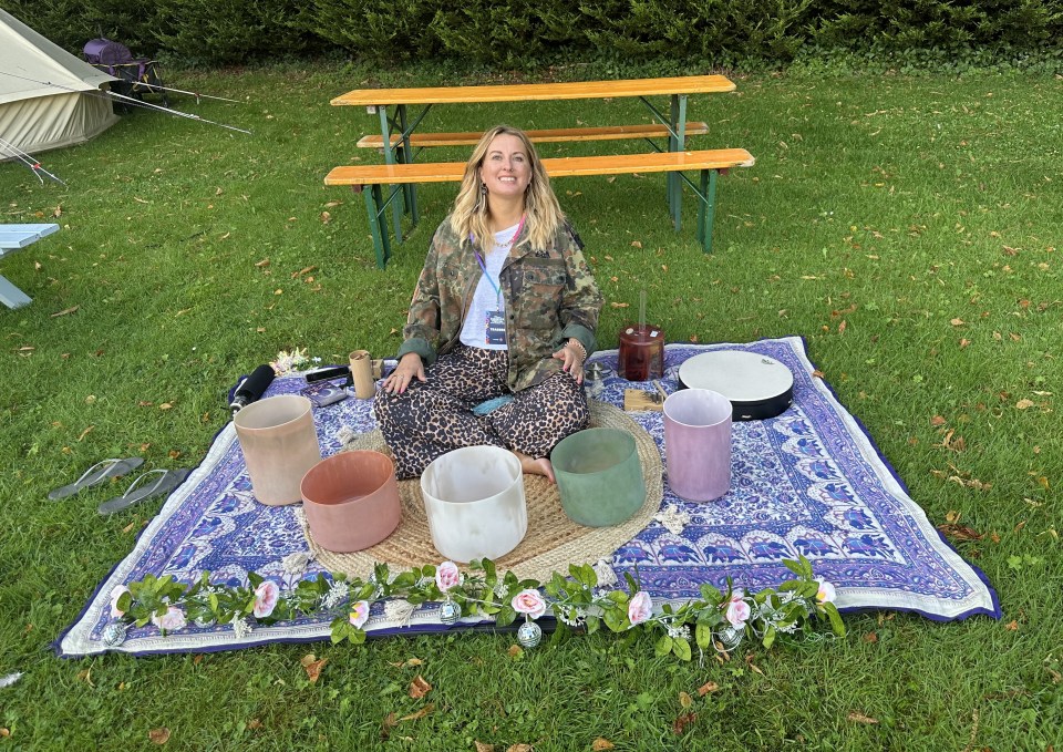 Woman sitting on a blanket outdoors playing singing bowls.