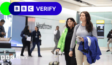 Two women at Heathrow airport, one holding a jacket over her arm and the other holding a suitcase.