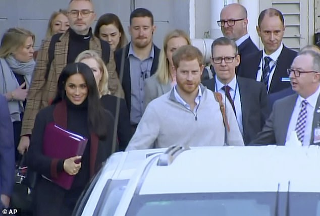 Prince Harry and his wife Meghan Markle, Duke and Duchess of Sussex, approach a car at an airport in Sydney surrounded by their entourage