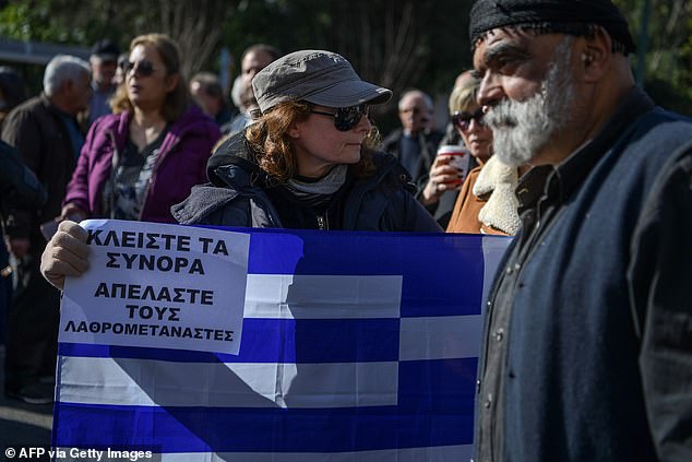 A woman holds a Greek flag and a placard reading 'Close the borders, Deport the illegal migrants' as she takes part in a demonstration against the governments plans to build new migrant camps on the islands
