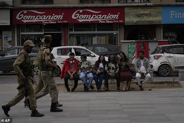 Indian tourists rests on a bench as policemen guard near a clock tower at the city centre in Srinagar