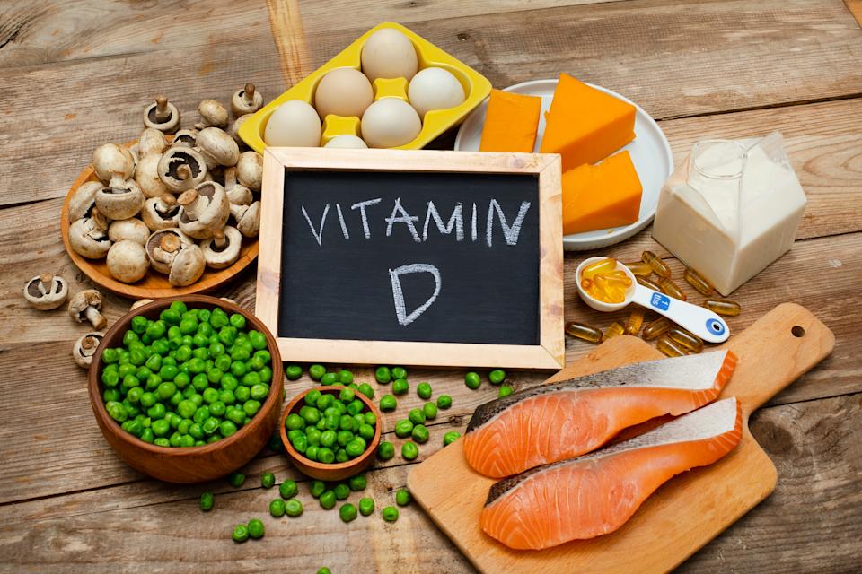 Fish, cheese, eggs, peas, and mushrooms arranged around a chalkboard labeled "Vitamin D" on a wooden table