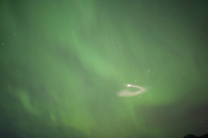 A vivid green aurora borealis shines in the night sky, with delicate curtains of light stretching across the scene. A few stars are visible, adding to the celestial display.