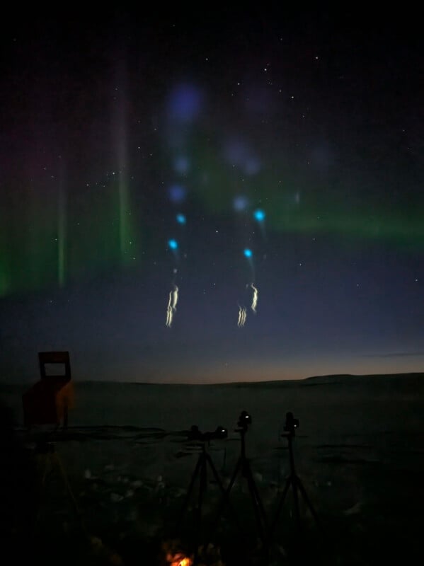 Night sky featuring auroras and bright, mysterious light formations resembling jellyfish. The foreground shows equipment set up on a snowy landscape, likely for sky observation or photography.