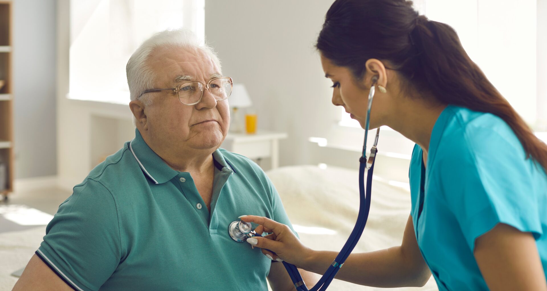Homecare nursing service and elderly people cardiology healthcare. Close up of young hispanic female doctor nurse check mature caucasian man patient heartbeat using stethoscope during visit