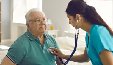 Homecare nursing service and elderly people cardiology healthcare. Close up of young hispanic female doctor nurse check mature caucasian man patient heartbeat using stethoscope during visit