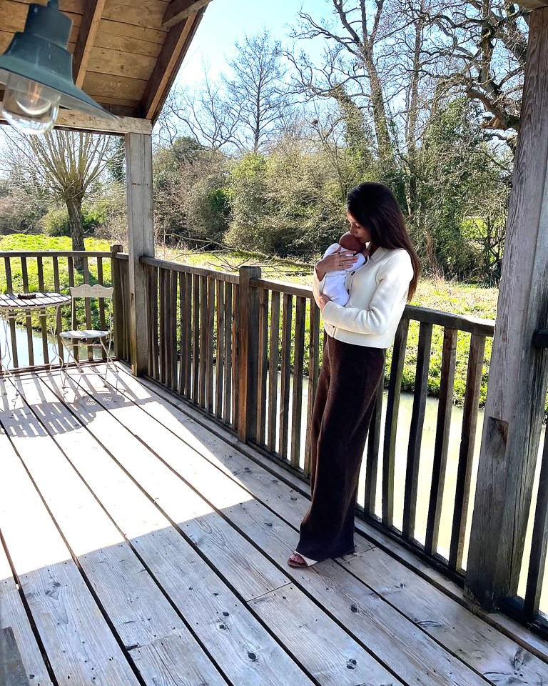 Woman holding a baby on a wooden deck overlooking a waterway.