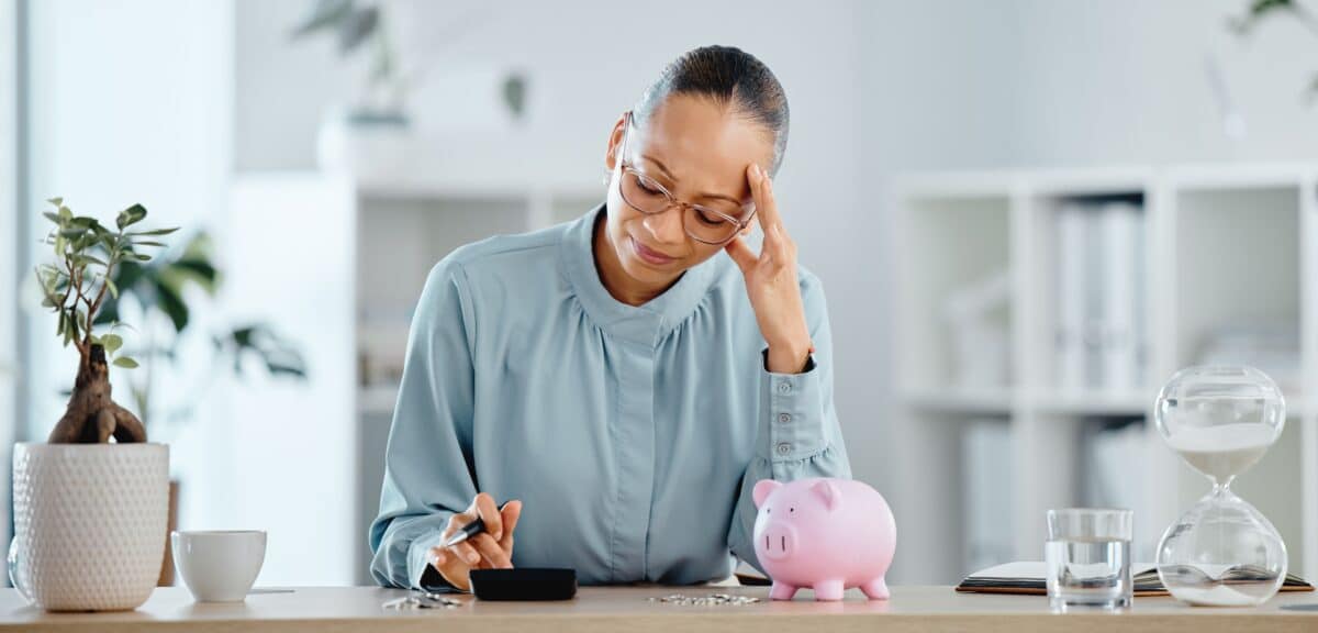 A woman stressed about her finances calculating her budget with a piggy bank