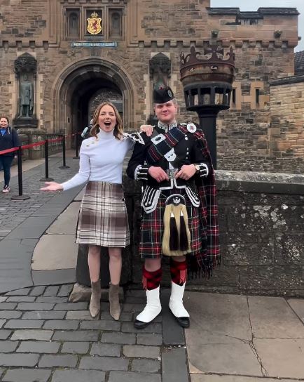 Woman in a kilt and a bagpiper in front of a castle.